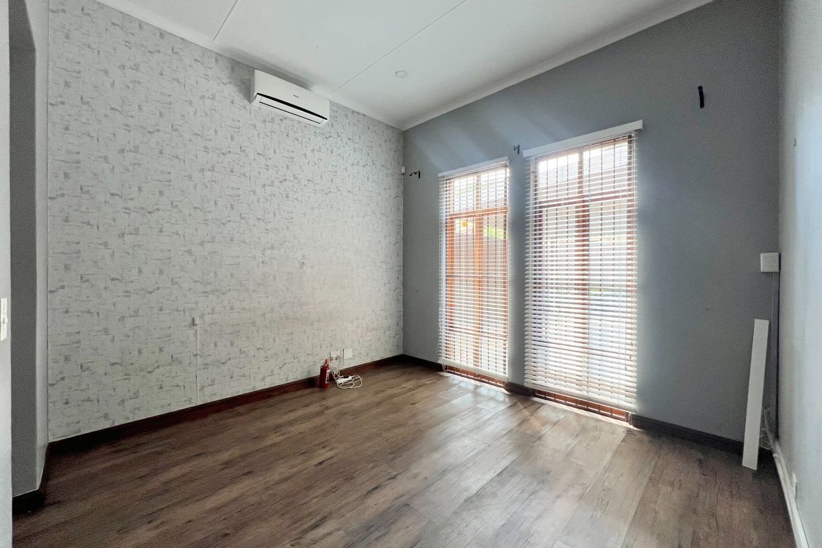 An empty bedroom featuring laminate flooring, split-system air conditioning, and dual windows with venetian blinds, offering a clean, neutral space ready for personalization.
