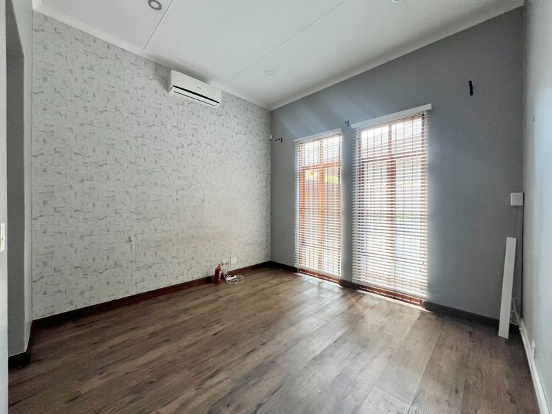An empty bedroom featuring laminate flooring, split-system air conditioning, and dual windows with venetian blinds, offering a clean, neutral space ready for personalization.