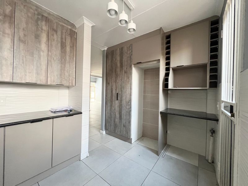 A modern, well-maintained scullery featuring neutral-toned built-in cabinetry, laminate countertops, tiled flooring, and dedicated appliance storage space.