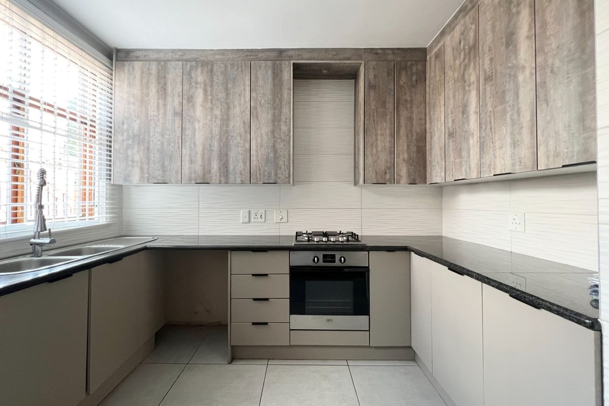 Modern kitchen featuring wood-look upper cabinetry, sleek granite countertops, built-in oven, gas hob, and tiled flooring with ample natural light.