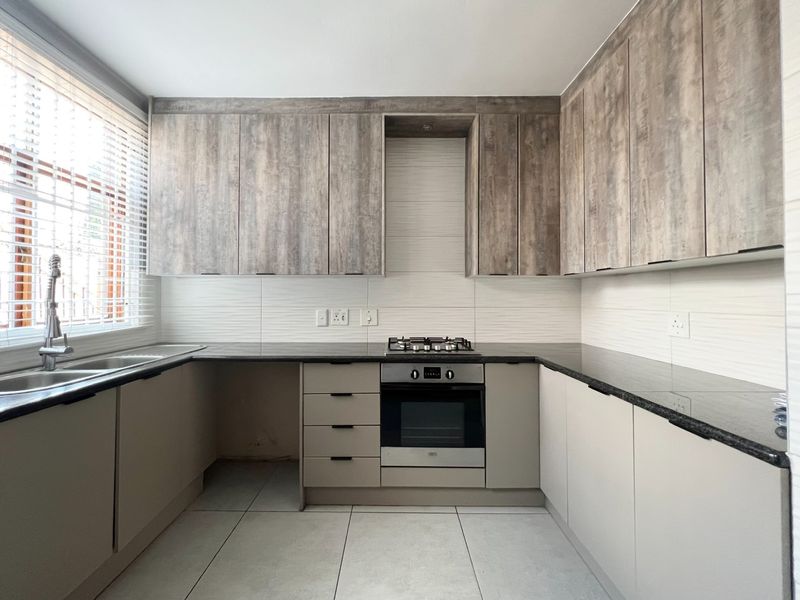 Modern kitchen featuring wood-look upper cabinetry, sleek granite countertops, built-in oven, gas hob, and tiled flooring with ample natural light.