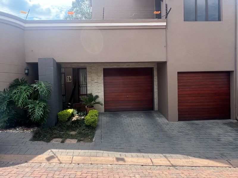 Front elevation of a townhouse featuring a double garage with wooden doors, paved driveway, and stone cladding accents.