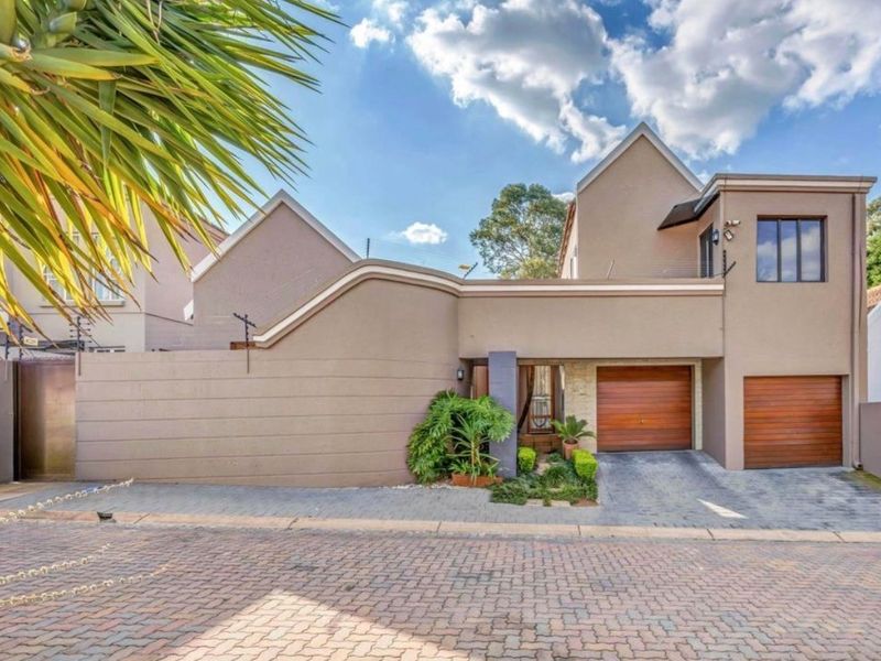 Front elevation of a modern townhouse featuring a double garage with timber doors, paved driveway, and secure boundary wall with electric fencing.