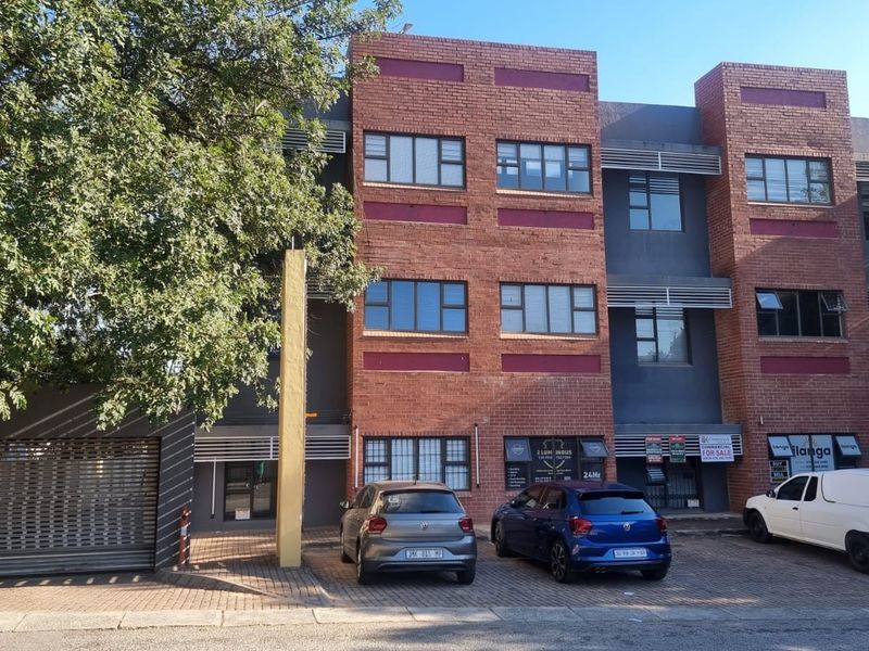 Front elevation of a multi-story commercial office building featuring a brick facade, aluminium windows, and dedicated paved parking spaces.