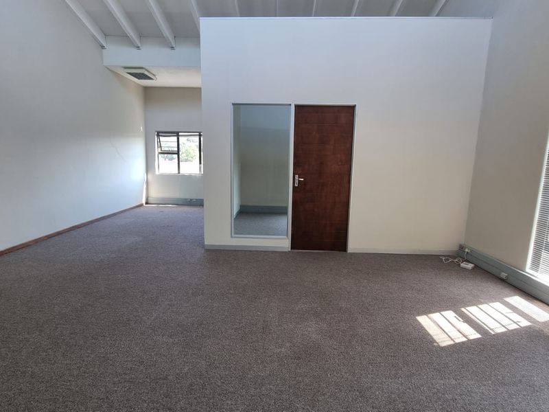 Spacious, empty office area featuring carpeted flooring, exposed ceiling beams, and natural light through multiple windows.
