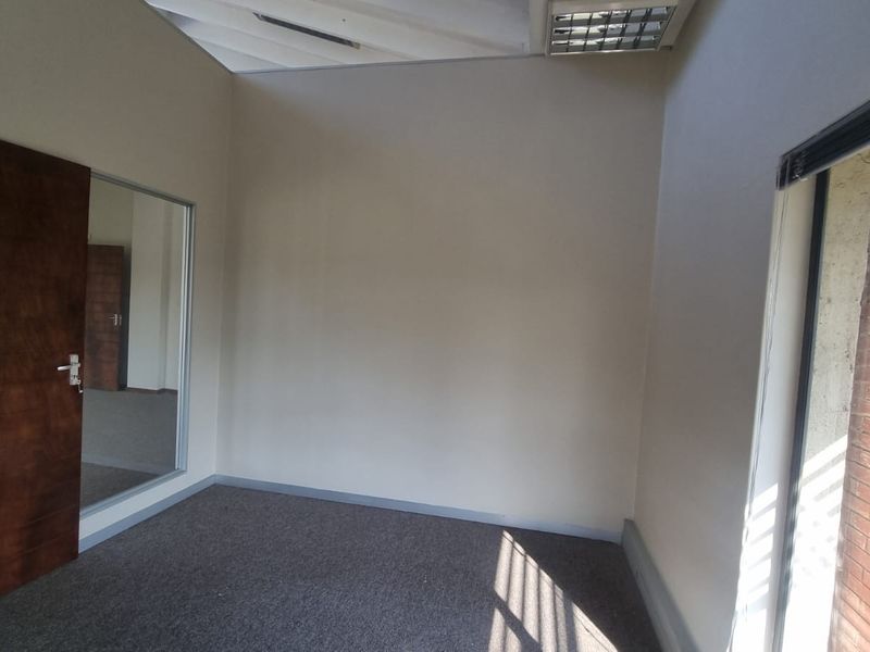 A bright, empty office space featuring carpeted flooring, a glass partition, and a timber door, suitable for a professional workspace.