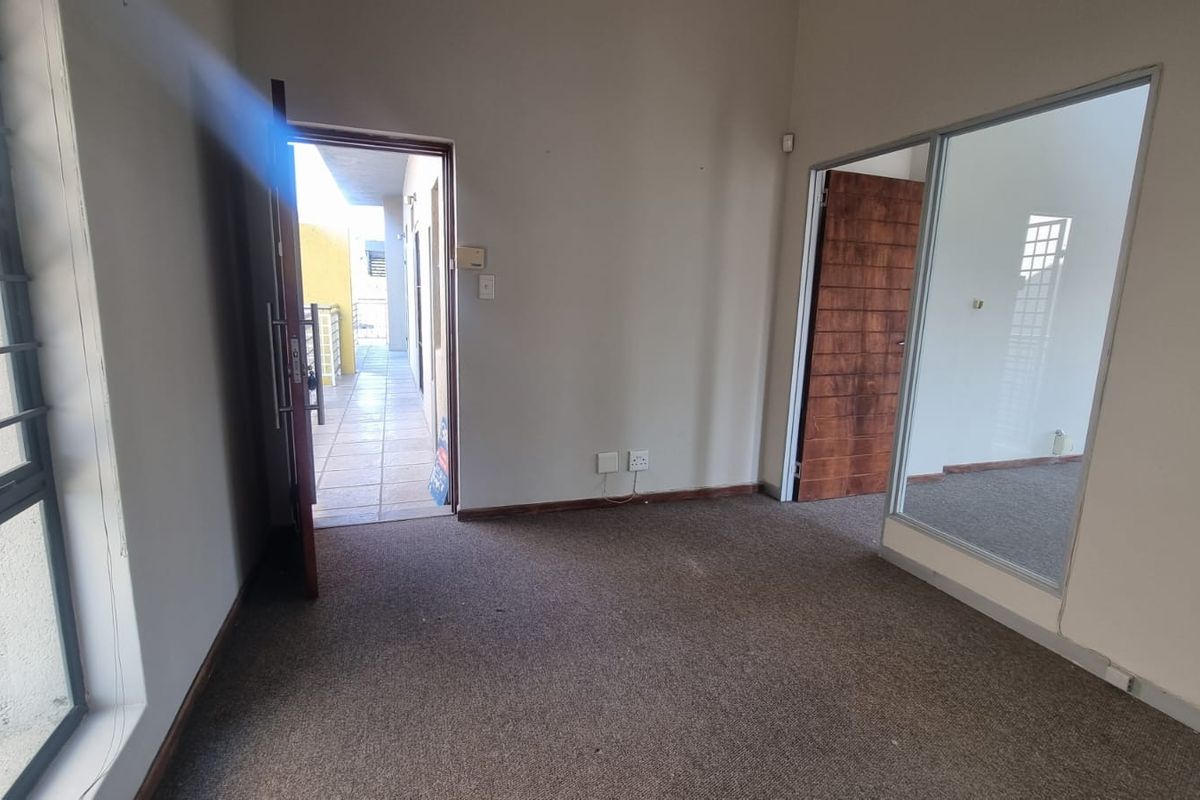 An empty office space featuring carpet flooring, a glass partition, and direct access to an external walkway.