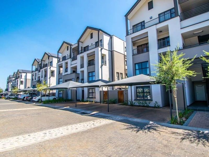 Exterior view of a modern multi-story apartment complex featuring paved parking areas with shade cloth carports and well-maintained building facades.