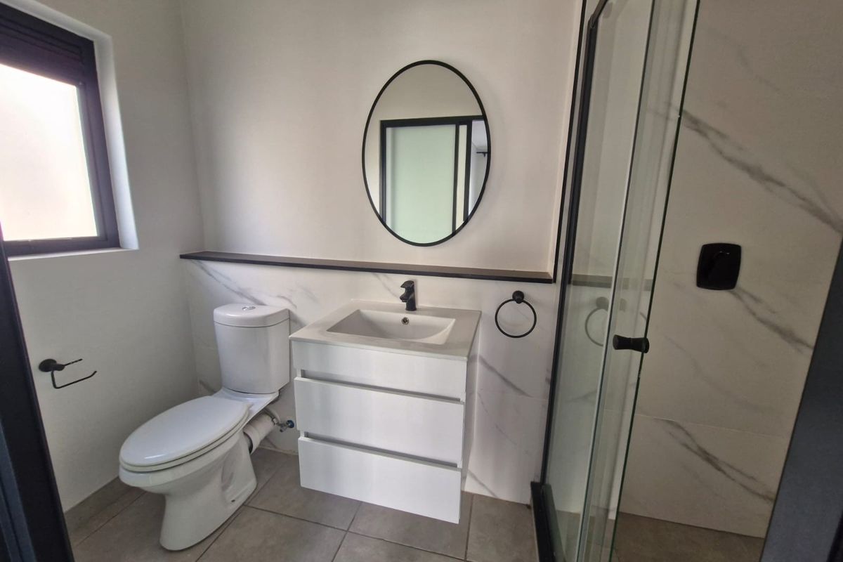 Modern bathroom featuring a sleek vanity, toilet, and glass-enclosed shower with contemporary black fixtures and marble-look wall tiling.