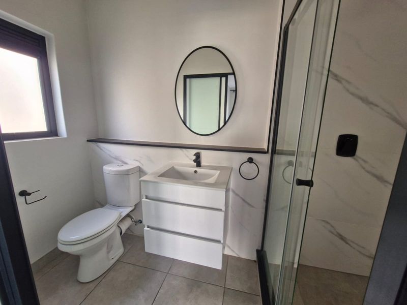 Modern bathroom featuring a sleek vanity, toilet, and glass-enclosed shower with contemporary black fixtures and marble-look wall tiling.