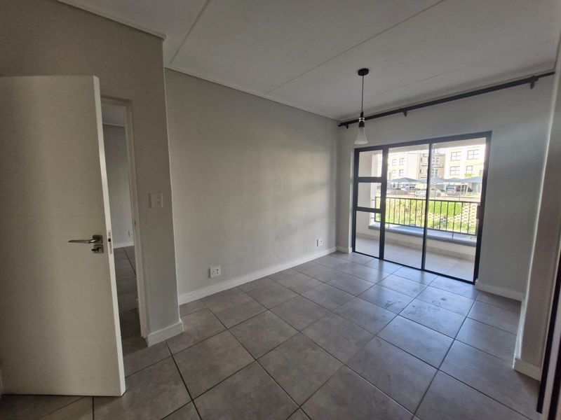 An empty, well-lit living area featuring neutral tiled flooring, modern skirting, and a sliding glass door providing access to a private balcony.