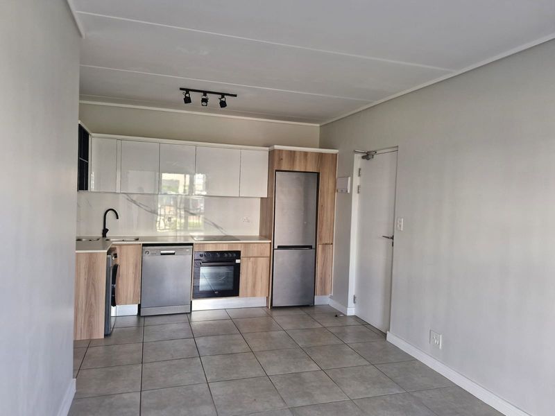 Modern open-plan kitchen featuring sleek white and wood-grain cabinetry, marble-look splashback, integrated appliances, and neutral tiled flooring in a clean, well-maintained space.