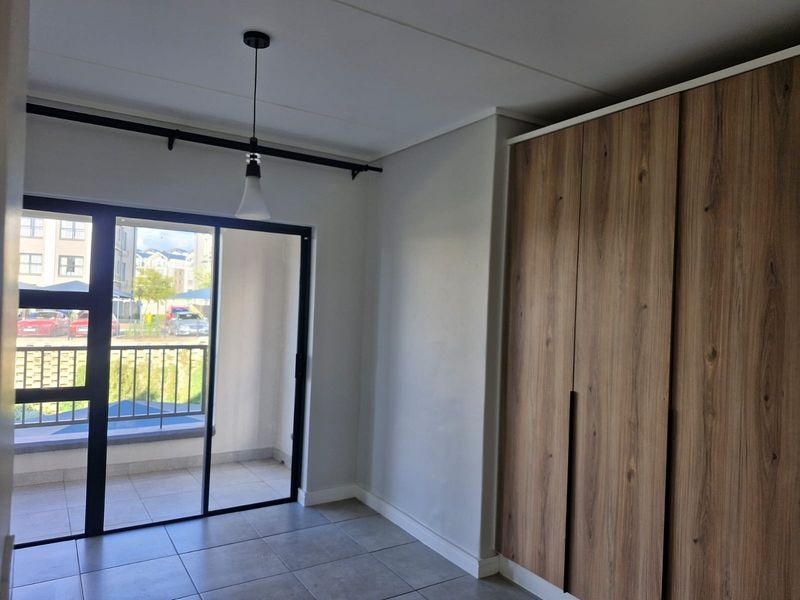 A bright, empty bedroom featuring modern wood-finish built-in cupboards, tiled flooring, and a sliding glass door leading to a private balcony.