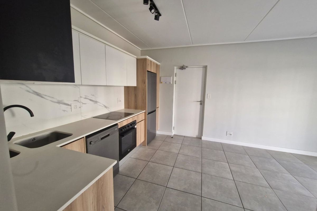 Modern kitchen featuring sleek white and wood-grain cabinetry, stone countertops, integrated appliances, and contemporary track lighting, set against neutral tiled flooring.