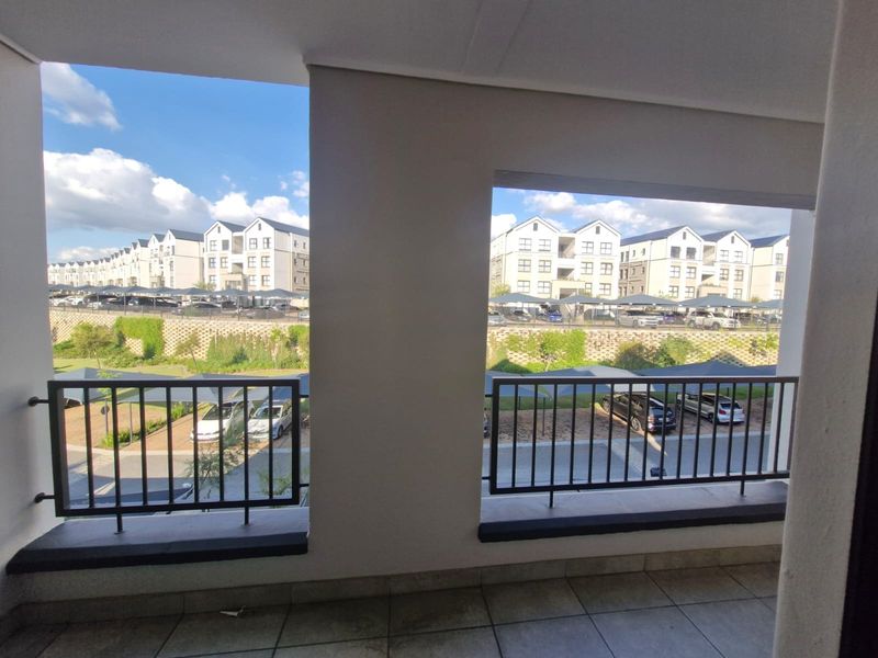 A covered balcony featuring tiled flooring and a metal balustrade, offering an elevated view of the surrounding apartment complex and parking area.