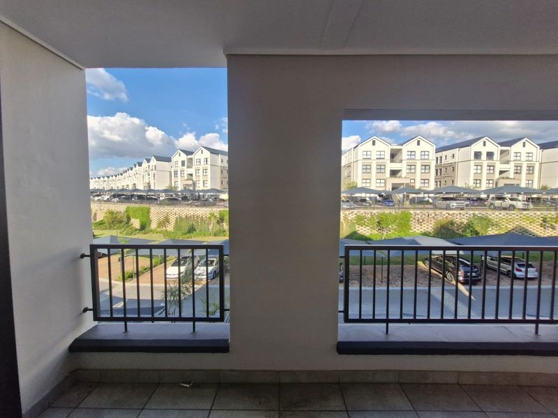 A covered balcony featuring tiled flooring and metal balustrades, offering an elevated view of the surrounding apartment complex and parking area.
