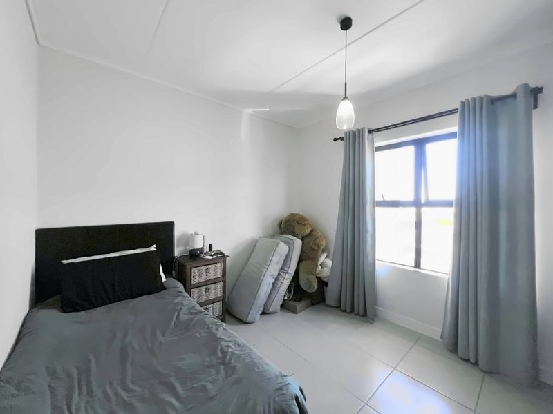 A bedroom featuring tiled flooring, a pendant light fixture, and an aluminium window frame with curtains.
