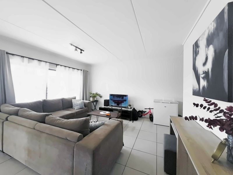 A bright and spacious living room featuring neutral tiled flooring, track lighting, and a large sliding glass door providing ample natural light.