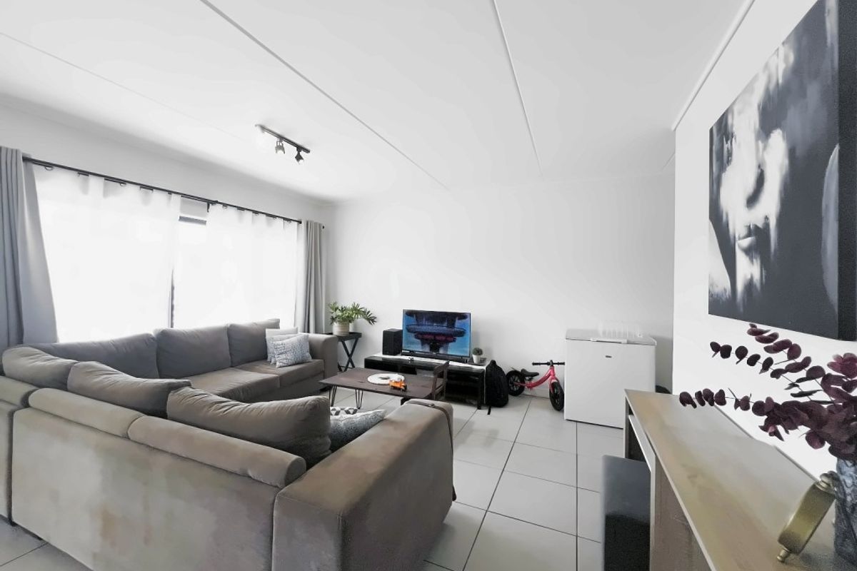 A bright and spacious living room featuring neutral tiled flooring, track lighting, and a large sliding glass door providing ample natural light.