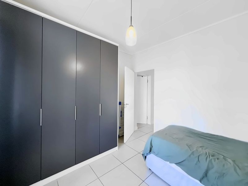 A clean bedroom featuring modern dark grey built-in cupboards, neutral tiled flooring, and a simple pendant light fixture.