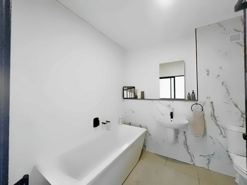Modern bathroom featuring a white bathtub, pedestal basin, and elegant marble-look wall tiling with a convenient built-in shelf.