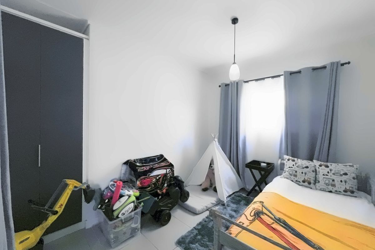A well-maintained bedroom featuring neutral tiled flooring, a built-in wardrobe, and a modern pendant light fixture, offering a clean and functional living space.