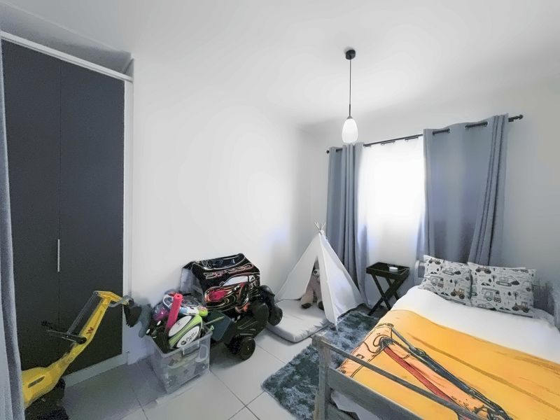 A well-maintained bedroom featuring neutral tiled flooring, a built-in wardrobe, and a modern pendant light fixture, offering a clean and functional living space.