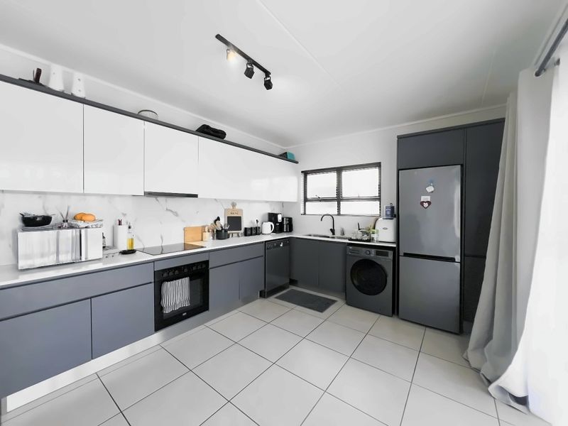 Modern kitchen featuring sleek two-tone cabinetry, marble-look splashback, integrated oven, electric hob, and tiled flooring with ample workspace.