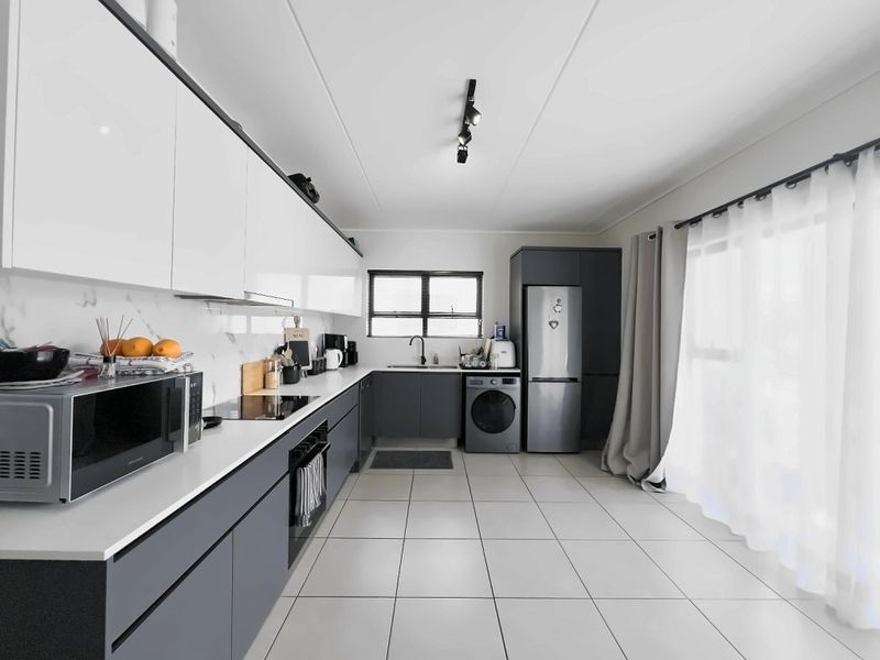Modern kitchen featuring sleek two-tone cabinetry, stone countertops, integrated appliances, and tiled flooring with ample natural light.