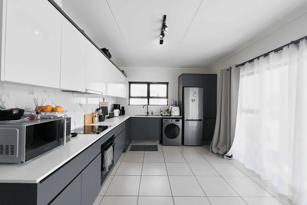 Modern kitchen featuring sleek two-tone cabinetry, stone countertops, integrated appliances, and tiled flooring with ample natural light.