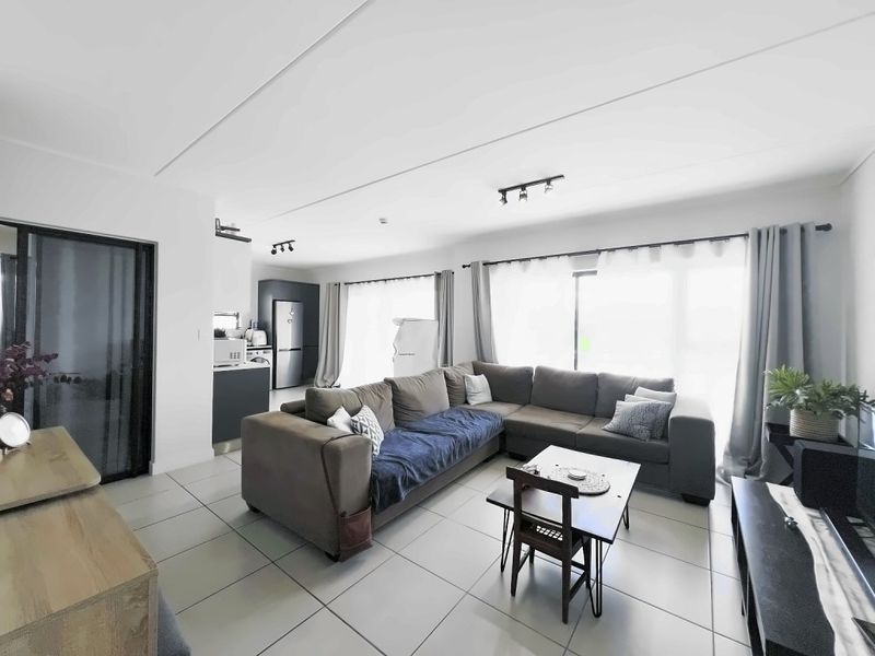 A bright open-plan living area featuring tiled floors, modern track lighting, and large sliding glass doors that provide ample natural light.
