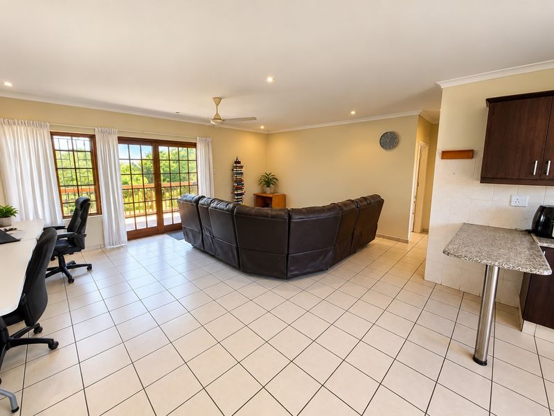 Spacious open-plan living area featuring tiled floors, a ceiling fan, and a functional kitchen with granite countertops and dark wood cabinetry.