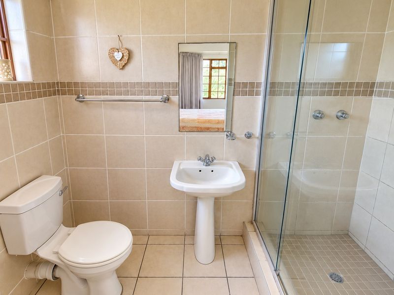 A functional bathroom featuring a pedestal washbasin, toilet, and a glass-enclosed shower with neutral ceramic wall and floor tiling.