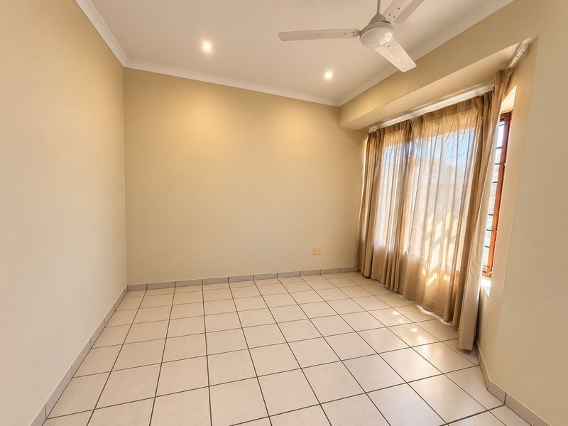 A bright, empty bedroom featuring neutral tiled flooring, a ceiling fan, and recessed lighting, ready for personalization.