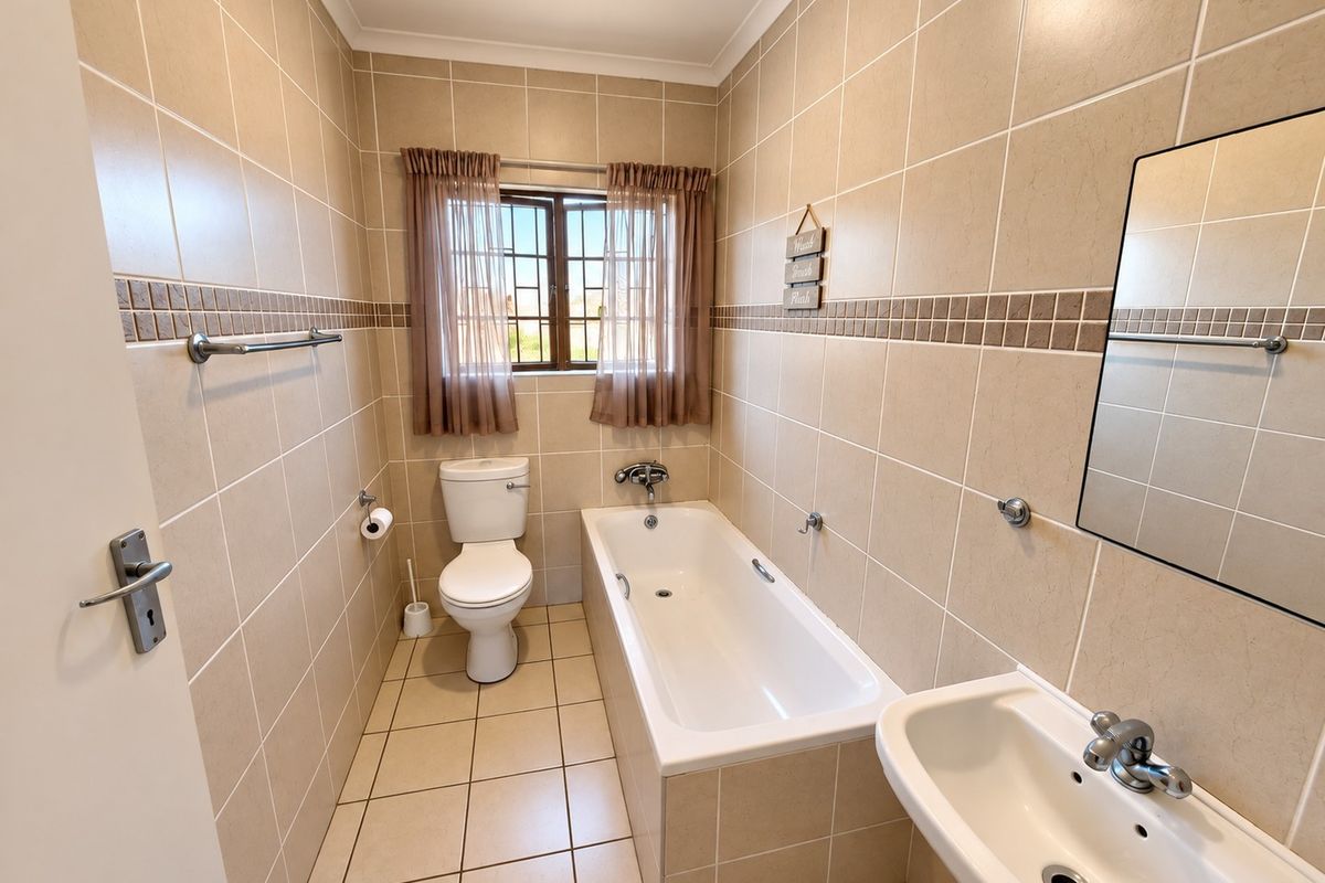 A clean, functional bathroom featuring neutral wall and floor tiles, a standard bathtub, pedestal basin, and a window for natural light.