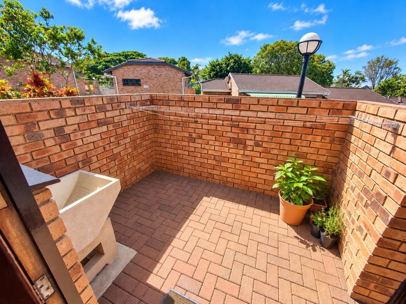 An outdoor laundry area featuring a brick-walled courtyard, paved flooring, and a built-in concrete wash trough with a wall-mounted clothesline.