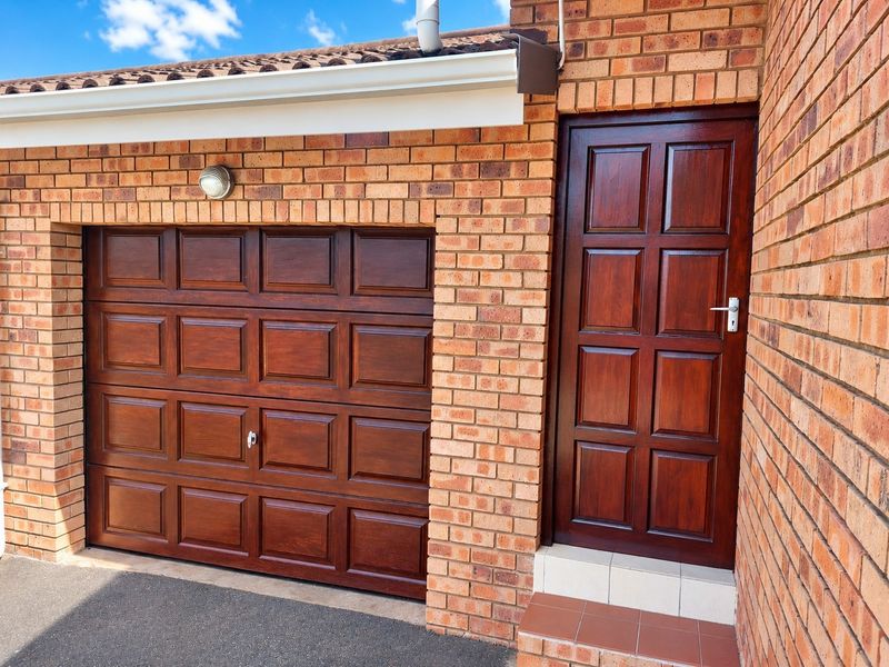 Exterior view of a townhouse garage featuring a dark wood-finish sectional door and a matching timber entrance door with tiled step.