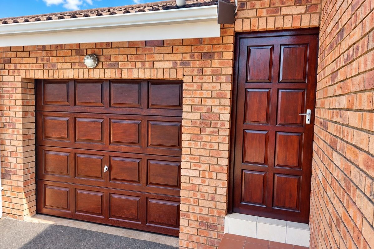 Exterior view of a townhouse garage featuring a dark wood-finish sectional door and a matching timber entrance door with tiled step.