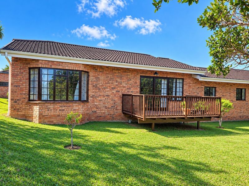Rear view of the townhouse featuring a classic brick facade, a raised timber deck, and a well-maintained lawn area.