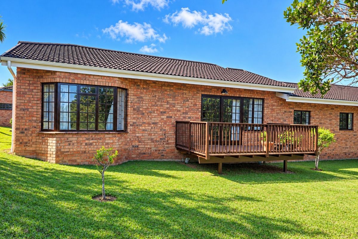 Rear view of the townhouse featuring a classic brick facade, a raised timber deck, and a well-maintained lawn area.