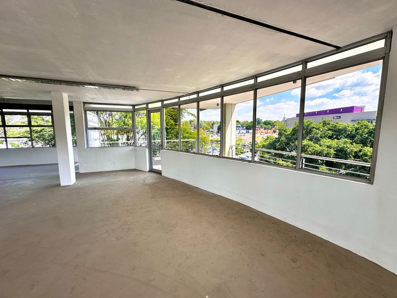 An open-plan office space featuring expansive windows with natural light, structural columns, and concrete flooring, offering a versatile layout for professional use.