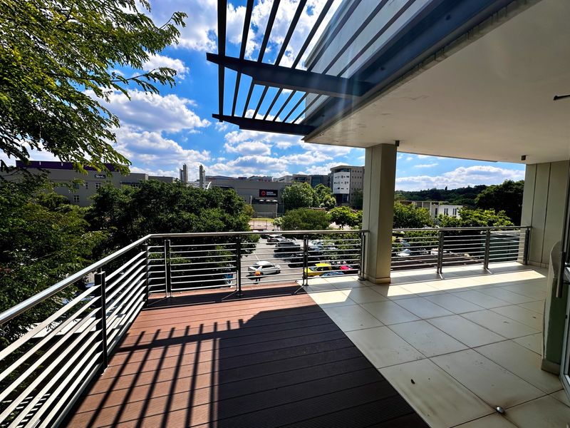 Spacious covered balcony featuring a mix of composite decking and tiled flooring, stainless steel railings, and a modern pergola structure overlooking the surrounding area.