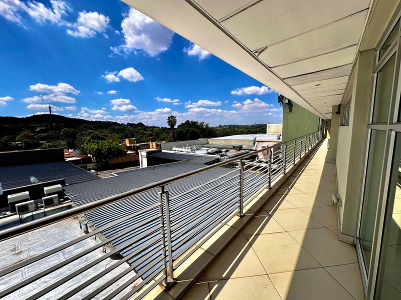 A spacious covered balcony featuring tiled flooring and a stainless steel balustrade, offering elevated views of the surrounding area.