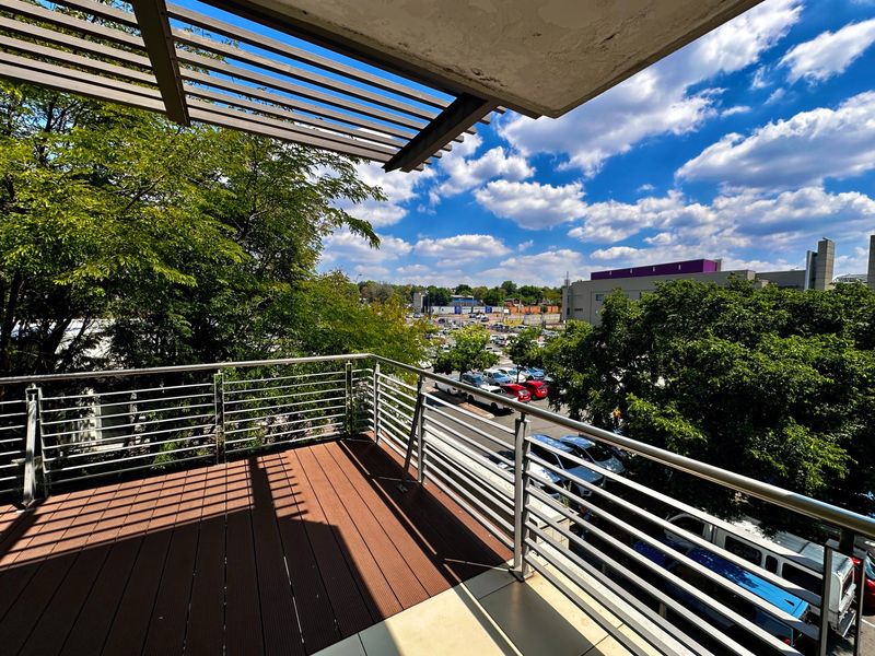 A modern balcony featuring timber decking, a stainless steel balustrade, and a slatted pergola, offering an elevated view of the surrounding area.
