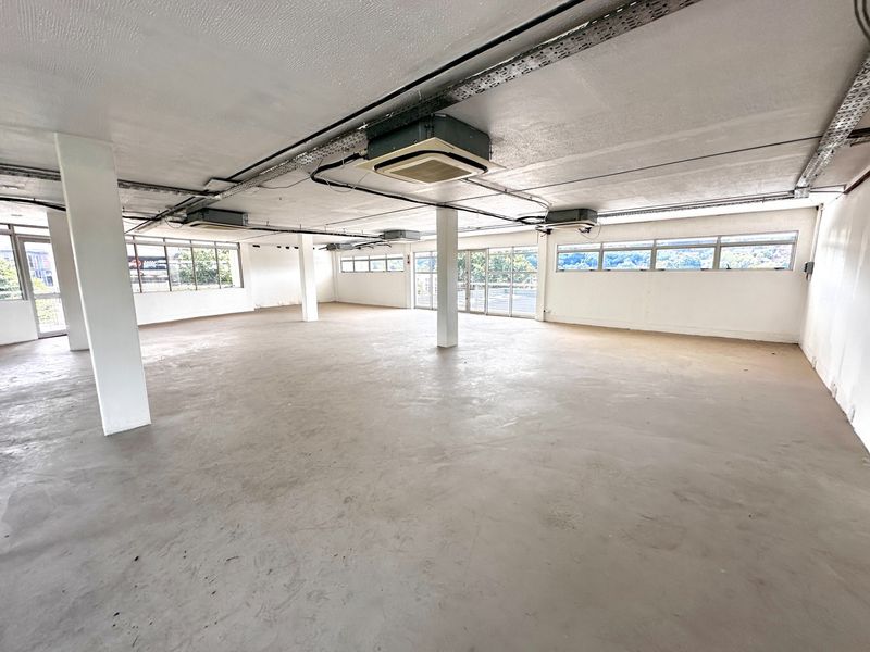 Spacious open-plan office area featuring exposed ceilings, ducted air conditioning, structural columns, and large windows providing ample natural light.