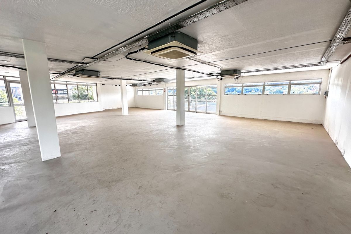 Spacious open-plan office area featuring exposed ceilings, ducted air conditioning, structural columns, and large windows providing ample natural light.