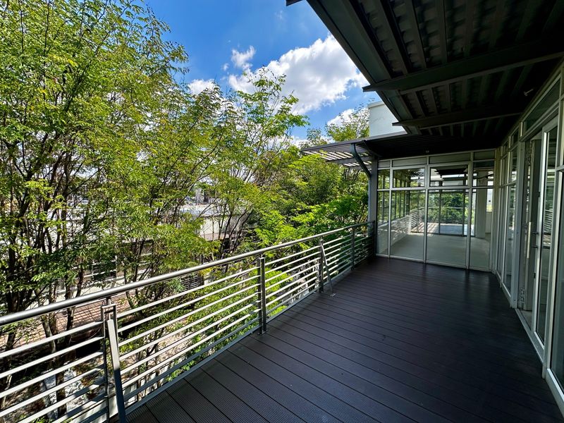 A spacious, modern balcony featuring dark composite decking, a sleek metal railing, and large glass sliding doors providing access to the office interior.