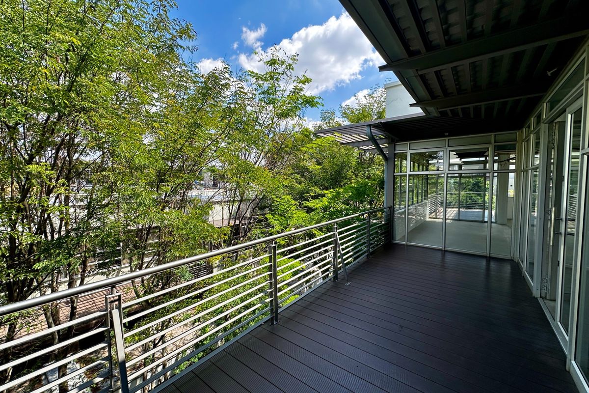 A spacious, modern balcony featuring dark composite decking, a sleek metal railing, and large glass sliding doors providing access to the office interior.