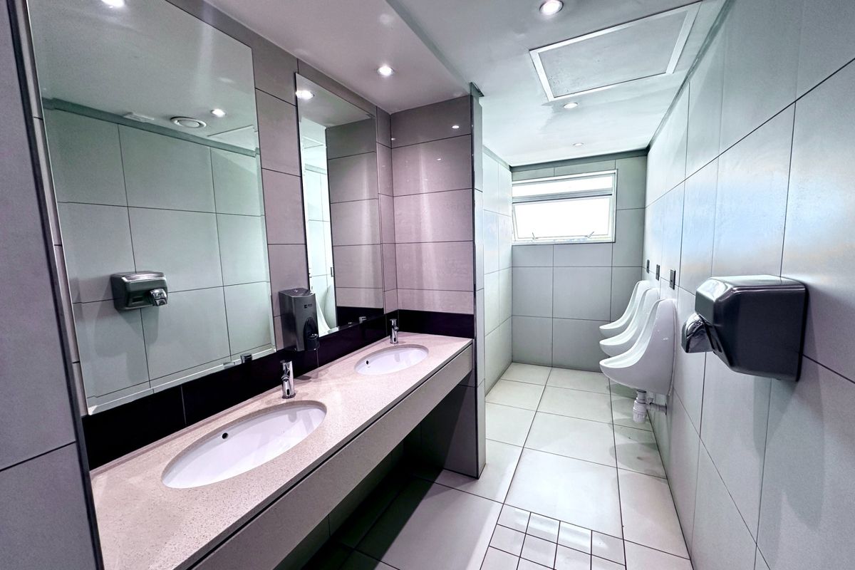 Modern office restroom featuring a dual vanity with stone countertop, tiled finishes, and multiple wall-mounted urinals.