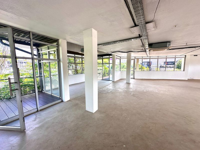 Spacious, open-plan office area featuring exposed ceiling cable trays, large windows for natural light, and direct access to a private balcony.